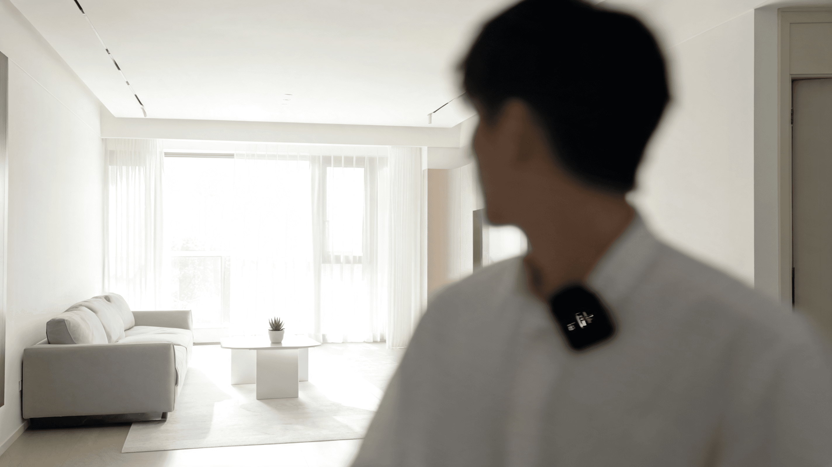 A clean, bright residential living room interior with a blurred human silhouette wearing a recording